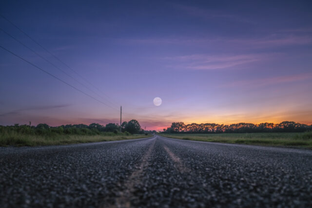 the sun is setting on the horizon of a road with a telephone pole in the foreground and trees in the background