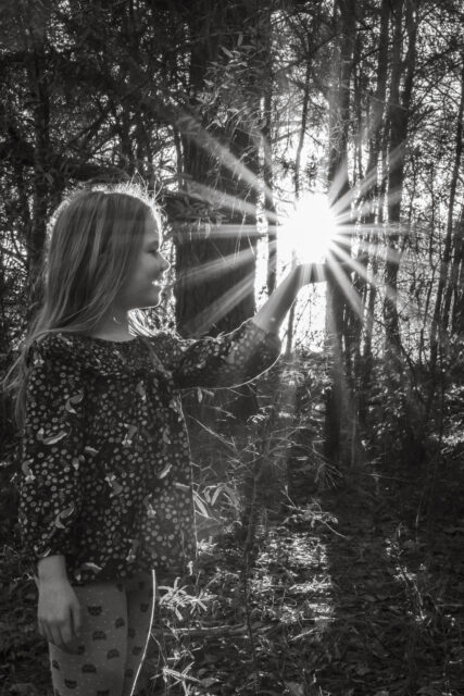 a girl standing in the woods with the sun shining through the trees and her hair blowing in the wind